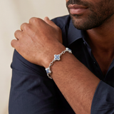 Man wearing a silver bracelet with a blue gemstone on a neutral background